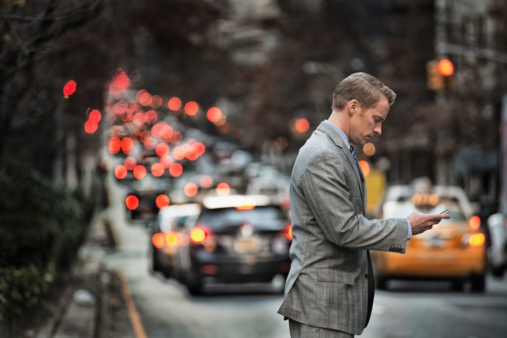 Man looking at his cell phone while cars pass by on the street.