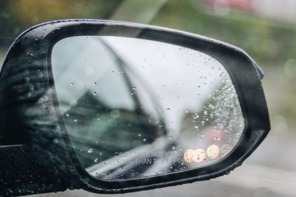 Passenger side mirror of a car driving in rain.